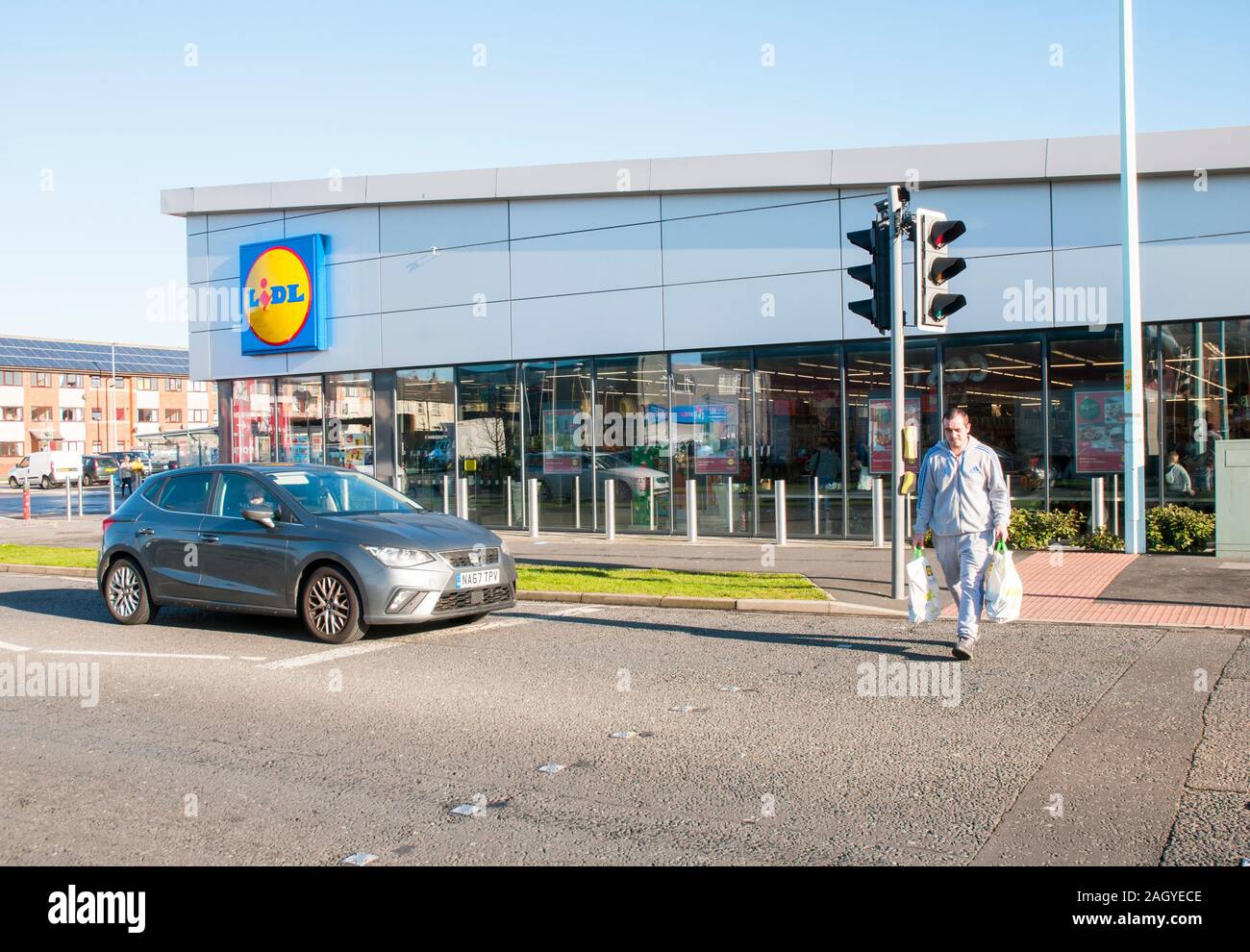 Neu gebaute Lidl in Blackpool verkaufen Kosten cuttring Elemente wie Getränke, Essen etc. Mann mit Shopping bnags Crossing Road. Auf ein papageientaucher Kreuzung. Stockfoto