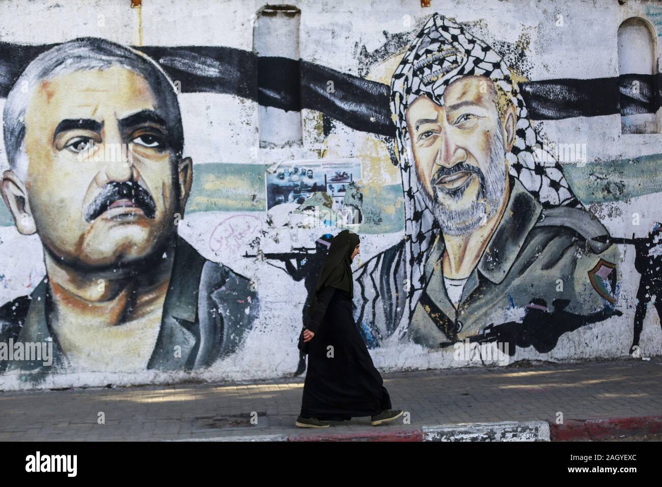 Gaza, Palästina. 22 Dez, 2019. Eine palästinensische Frau geht hinter einem Wandgemälde, das die verstorbenen Palästinenserführer Jassir Arafat und der Führer der Volksfront, George Habash in Gaza Stadt. Credit: Mahmoud Issa/SOPA Images/ZUMA Draht/Alamy leben Nachrichten Stockfoto