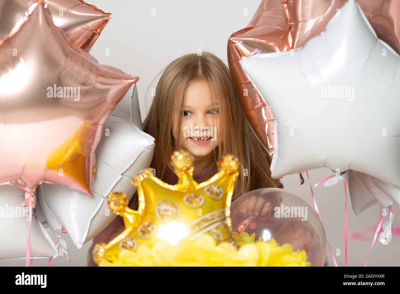 Blauäugigen blonden lacht und zeigt erste Zahn. Nettes Mädchen auf weißem Hintergrund und Ballons Stockfoto