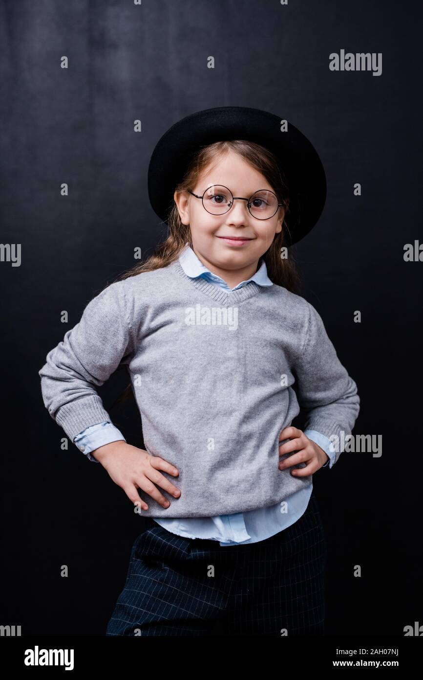 Hübsches kleines Mädchen in Smart Casual Wear und Brillen vor der Kamera auf schwarzem Hintergrund stehend Stockfoto