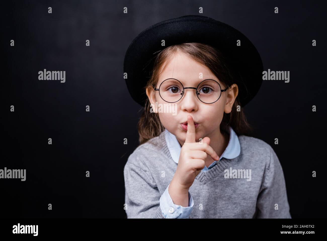 Adorable kleinen Mädchen in Smart Casual Wear und Brillen fragen Sie ruhig auf schwarzem Hintergrund isoliert zu halten. Stockfoto