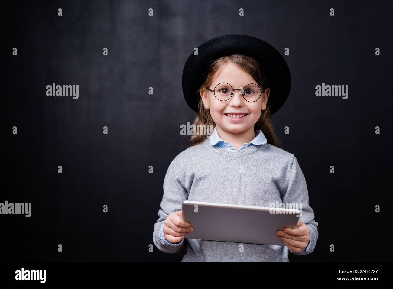 Hübsches kleines Mädchen in Smart Casual Wear und Brillen mit Touchpad beim Stehen vor der Kamera auf schwarzem Hintergrund Stockfoto