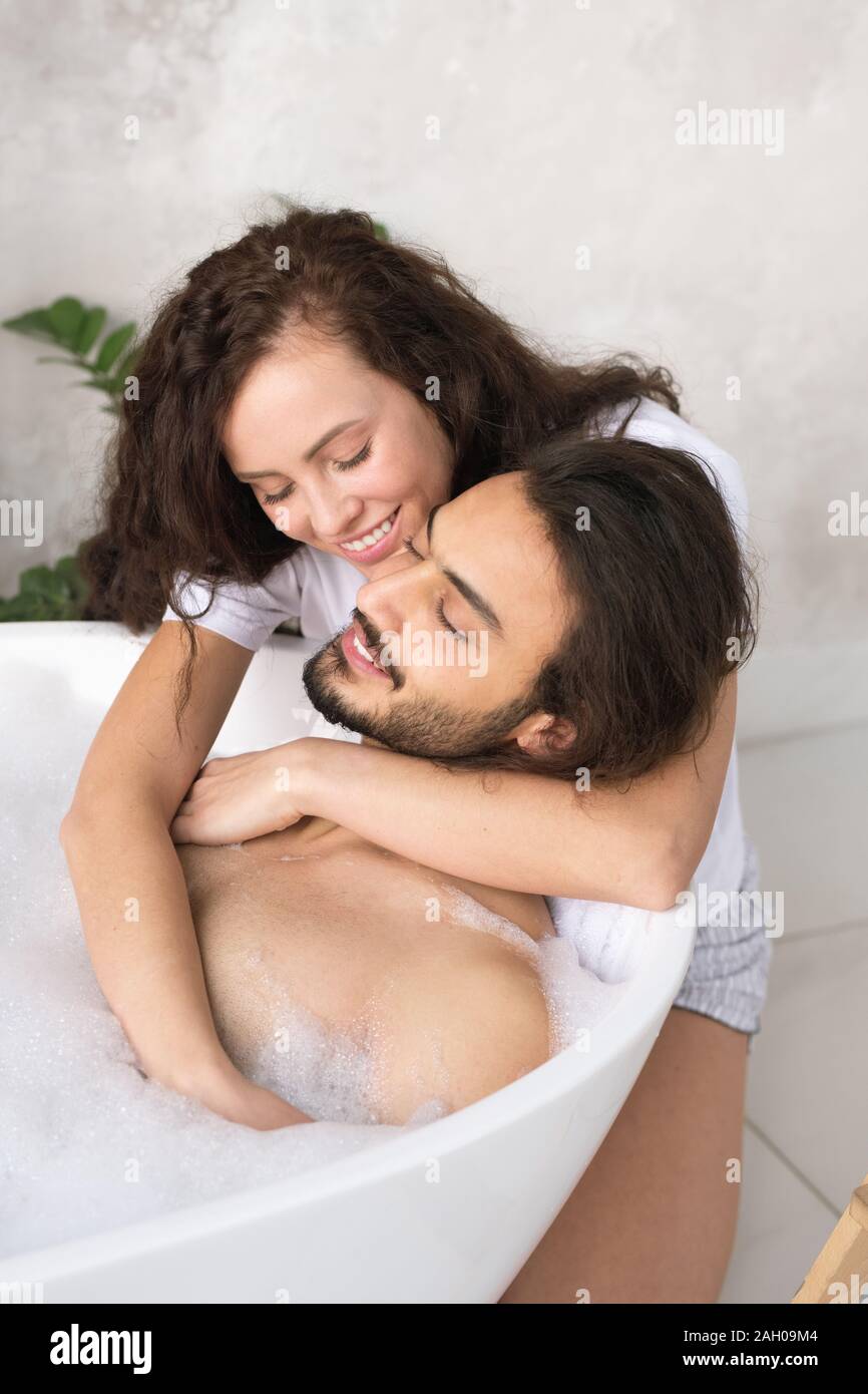 Glückliche junge liebevolle Frau, die ihren Mann entspannt genießen, Badewanne mit heißem Wasser und Schaum Stockfoto