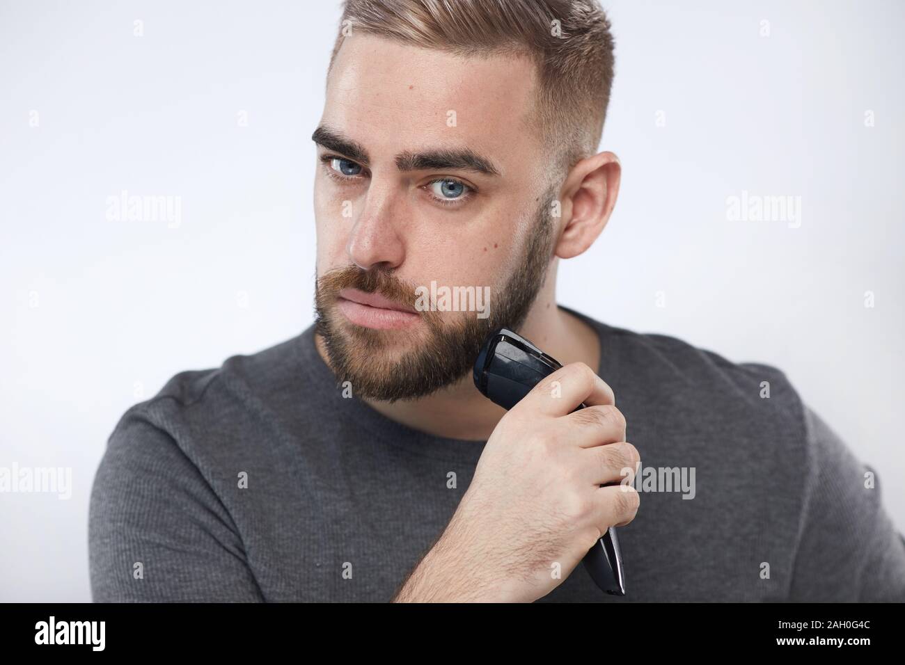 Kaukasischen jungen Mann Pflege mit seinen Bart Trimmer an Kamera horizontale Studio Portrait suchen Stockfoto