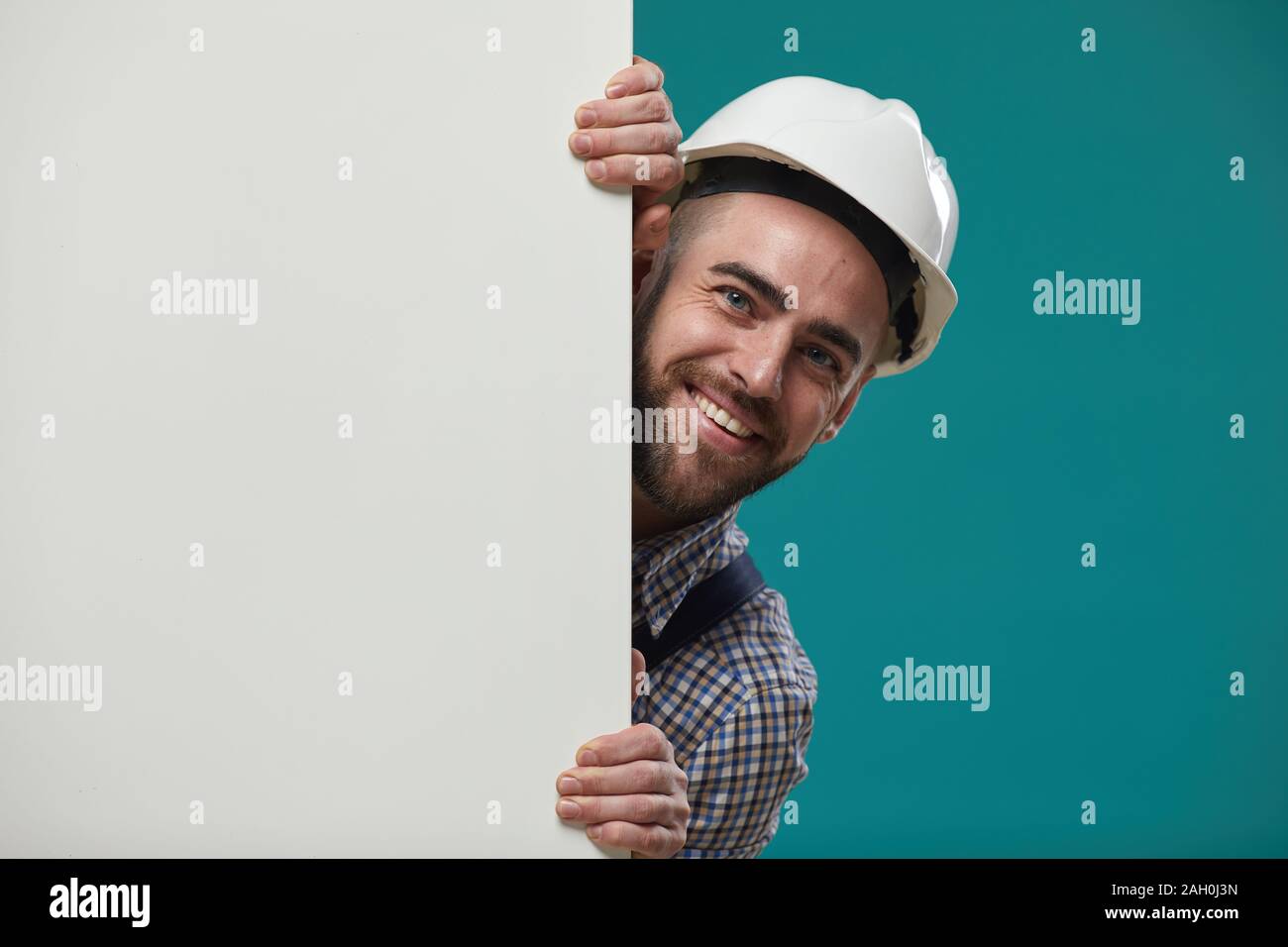 Horizontale medium Nahaufnahme von Happy Bauarbeiter tragen weiße hardhat Zusammenführung von hinten blank Billboard lächelnd, Kopie Raum Stockfoto