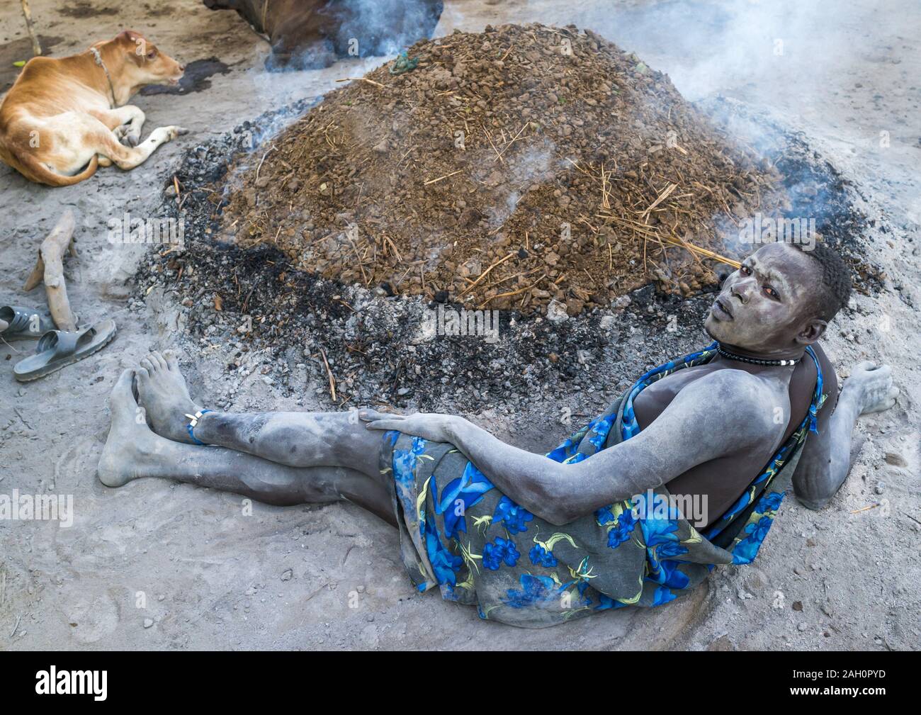 Mundari Stamm Mann Ruhe vor einem Lagerfeuer gemacht mit getrockneten Kuh dungs Mücken abzuwehren, Central Equatoria, Terekeka, South Sudan Stockfoto