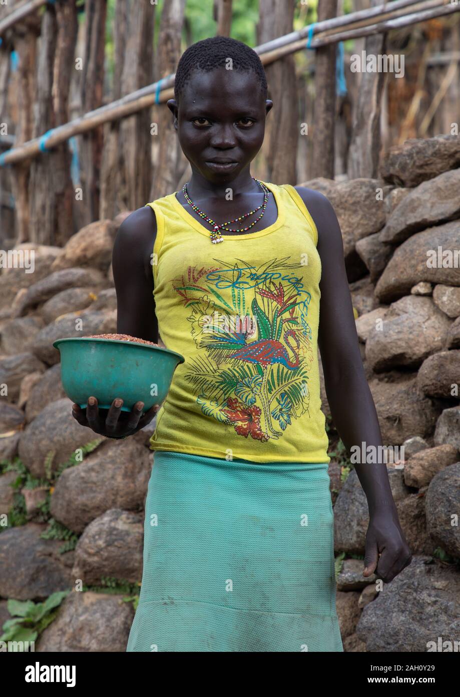 Lotuko Stamm Frau, die Essen vor einer Mauer aus Stein, Central Equatoria, Illeu, South Sudan Stockfoto