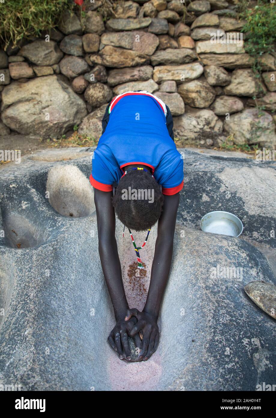 Lotuko Stamm Frau Schleifen Körner in ein Loch im Felsen, Central Equatoria, Illeu, South Sudan Stockfoto