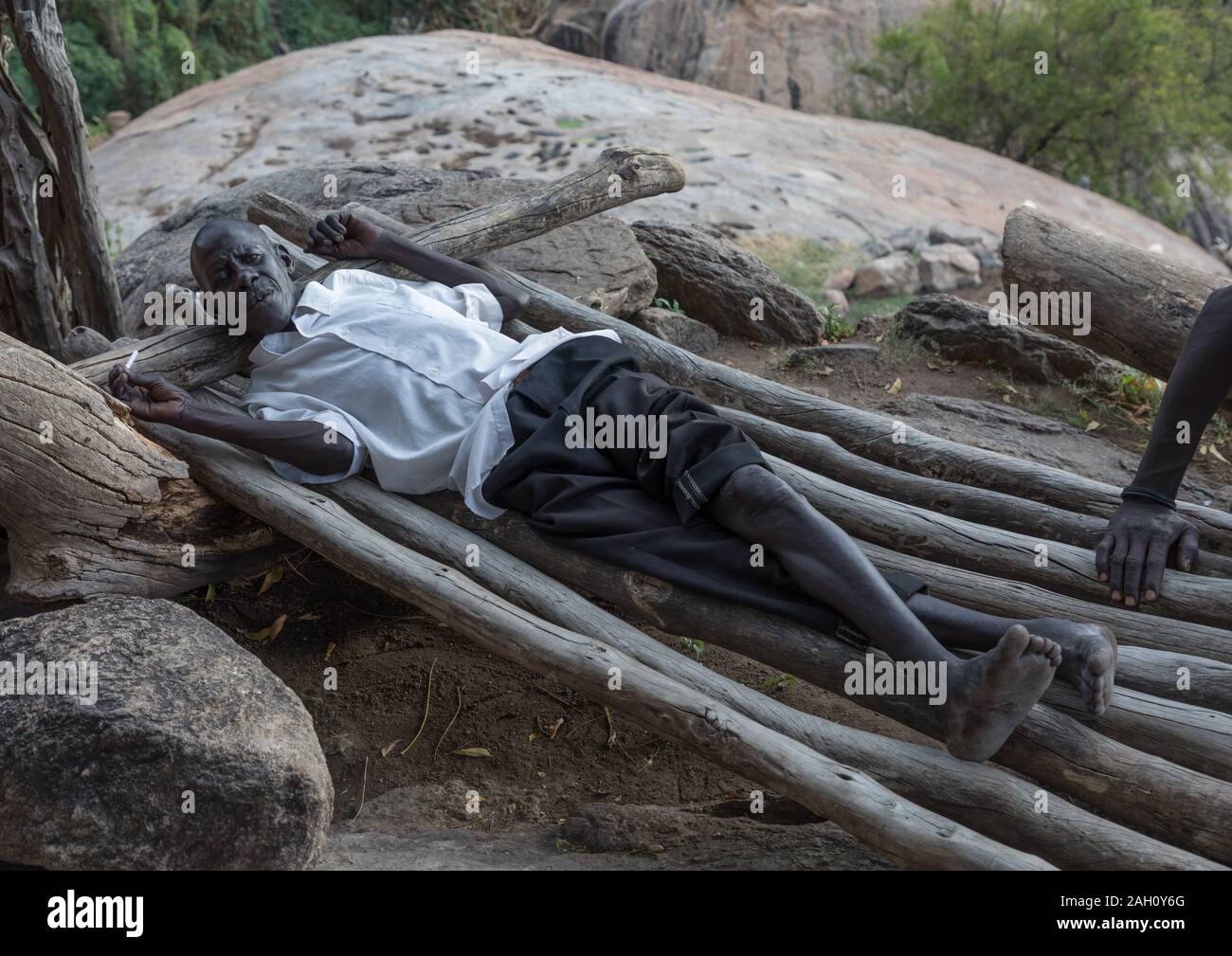 Lotuko Stamm Mann ruht auf einem Holz Bett, Central Equatoria, Illeu, South Sudan Stockfoto