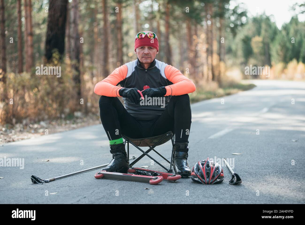 Training ein Athlet auf der Walze Skater. Biathlon Fahrt auf dem Roller Ski mit Skistöcke, im Helm. Athlet ist immer bereit zu starten. Herbst Stockfoto