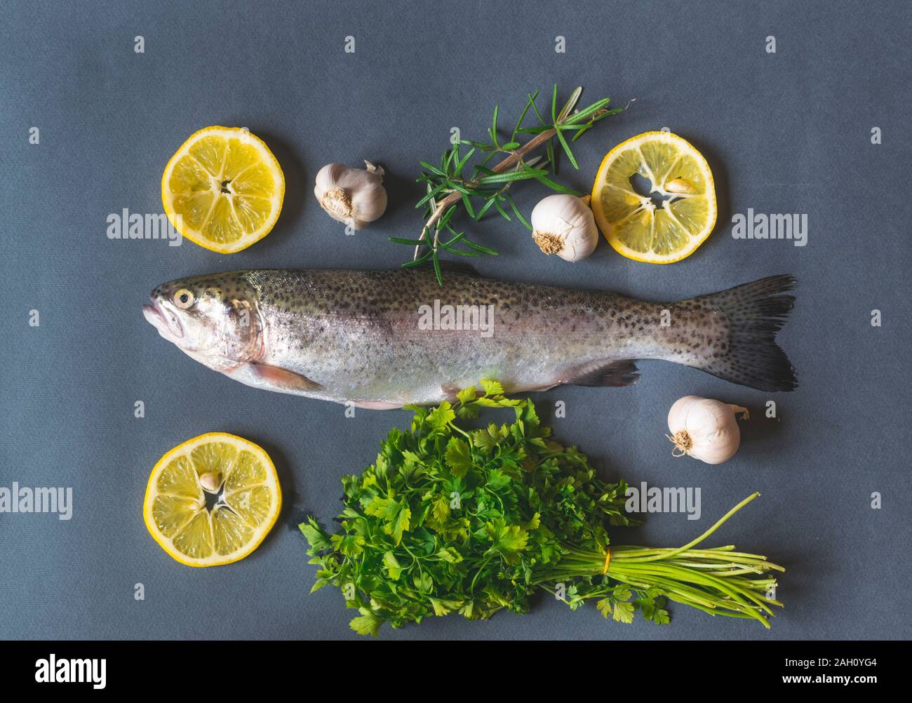 Frische Forellen auf dunklen Tisch mit Petersilie, Knoblauch und Rosmarin. Lecker Fisch vorbereiten für das Essen. Top Winkel anzeigen Stockfoto