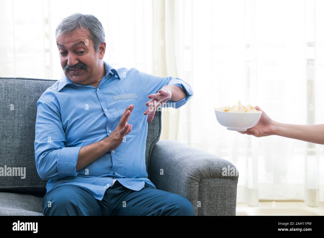 Porträt von einem älteren Mann zu Hause sitzen und sich von der Schüssel Chips. Stockfoto