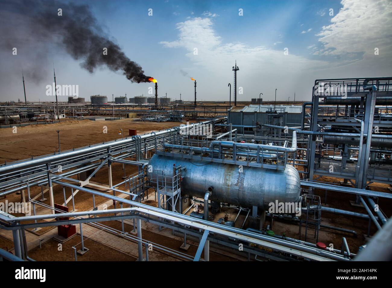 Grauen Rohre und orange Brennen Gasbrenner einer Ölraffinerie in der gelben Wüste. Blauer Himmel mit Wolken. Panorama Ansicht Stockfoto