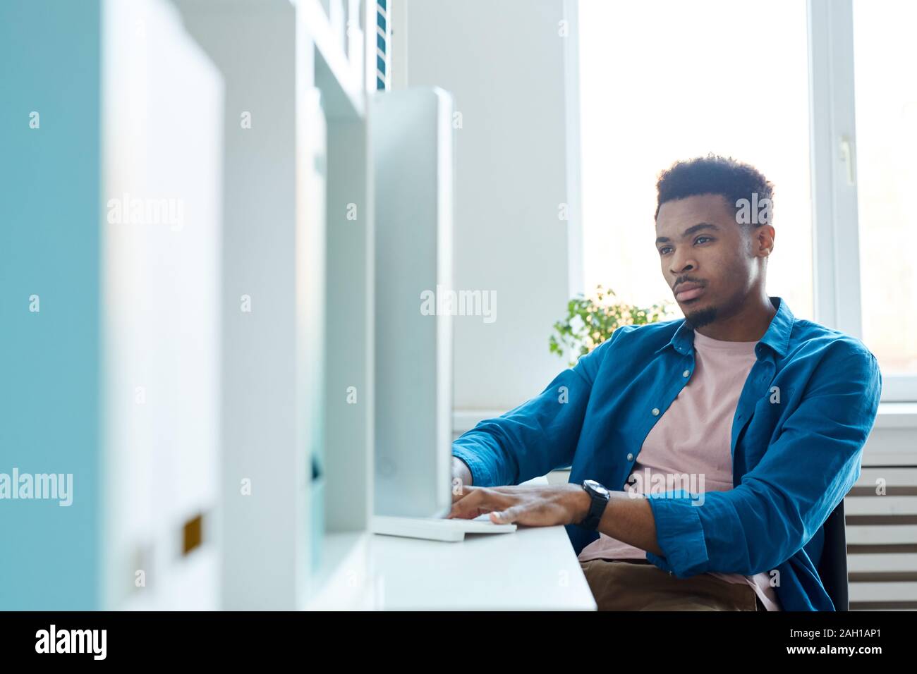 Schweren afrikanischen Mann in Freizeitkleidung sitzen am Tisch und die Eingabe über die Tastatur, die er auf dem Computer im Büro arbeiten Stockfoto