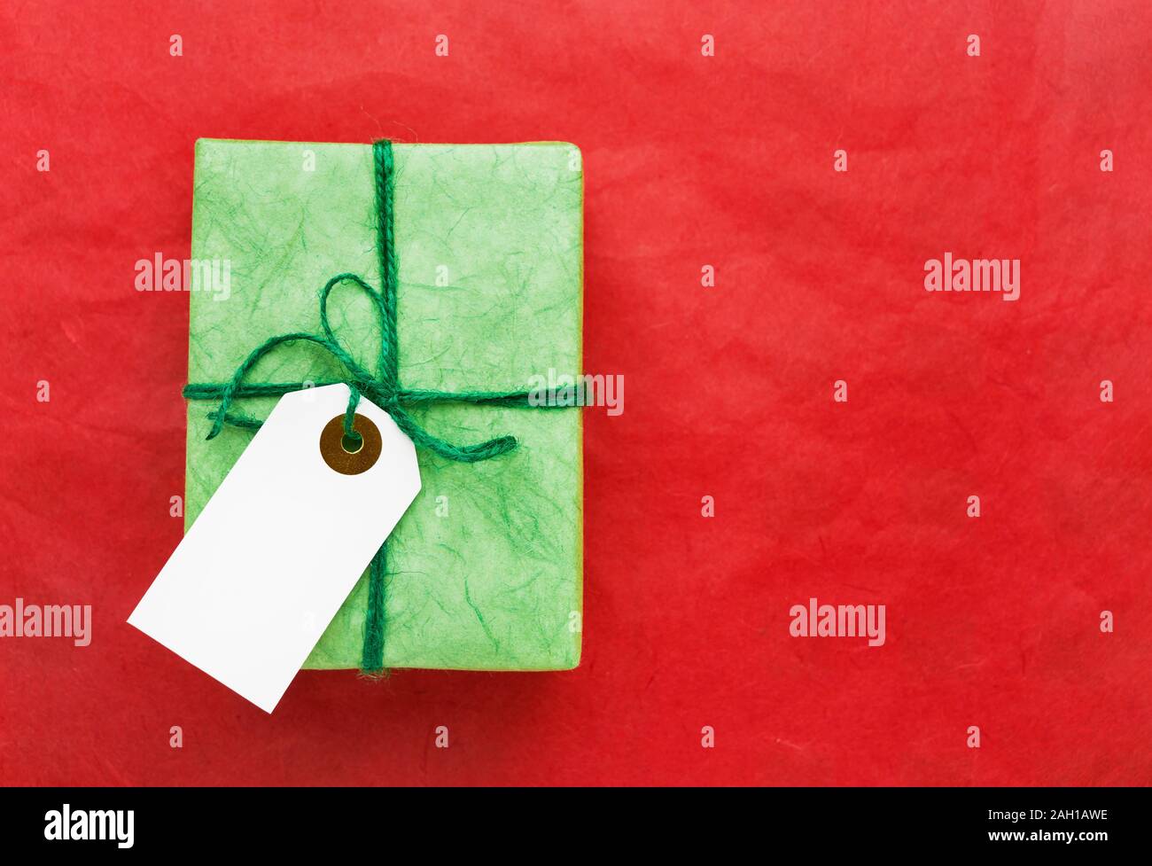 Grüne Geschenkbox mit weißen Geschenk tag auf rotem Hintergrund. Urlaub Konzept. Kopieren Sie Platz für Text, Ansicht von oben. Stockfoto