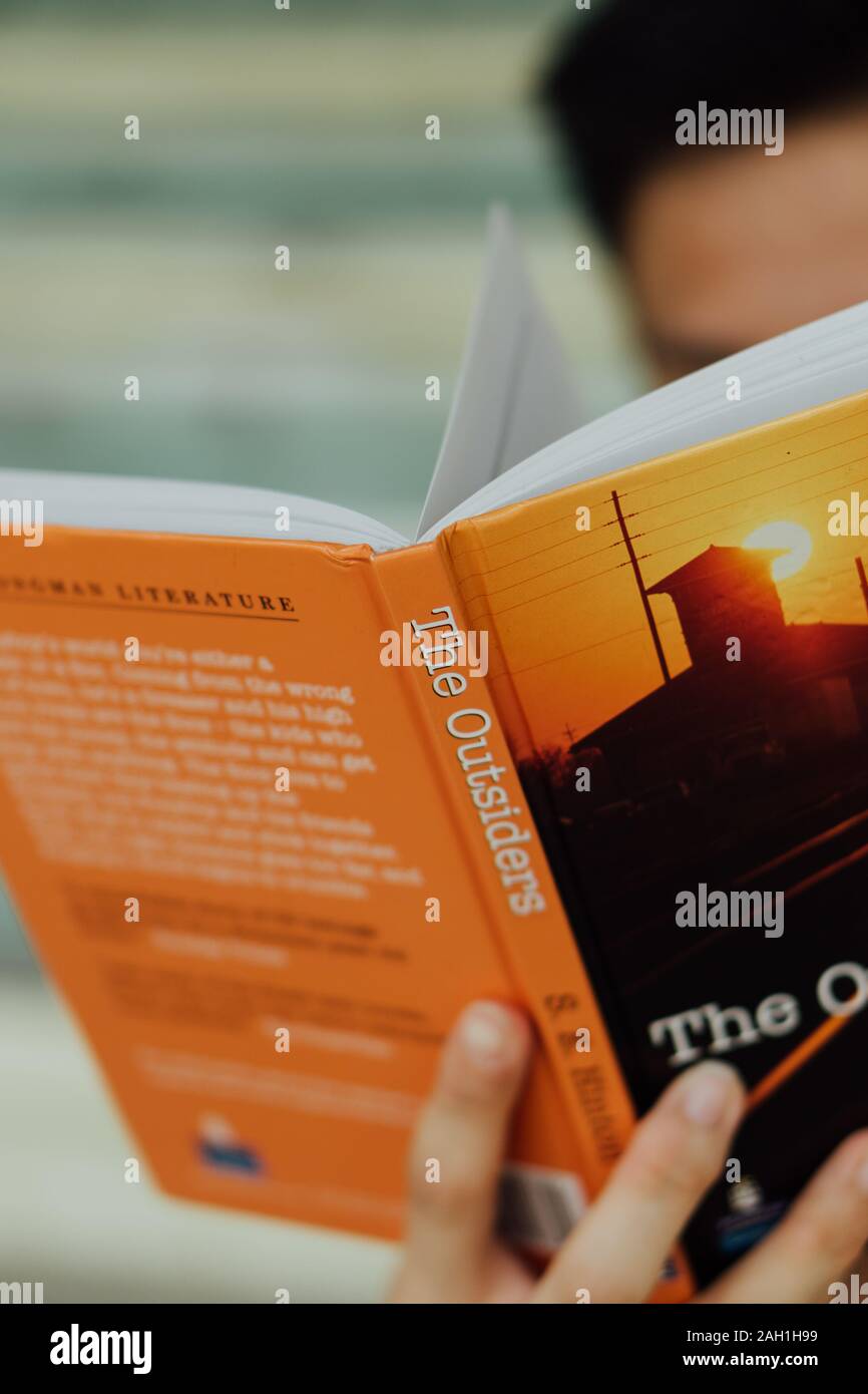 Singaporean männlichen Lesen ein Hardcover version Der Außenseiter Stockfoto