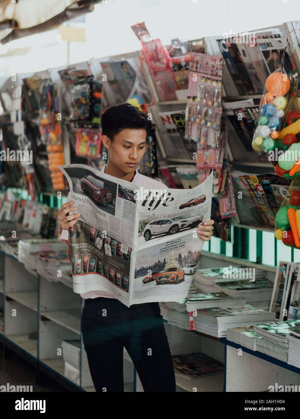 Singaporean männlichen lesen Abschnitt der Straße-Zeiten "Leben" in einer Zeitschrift/Zeitung Shop Stockfoto