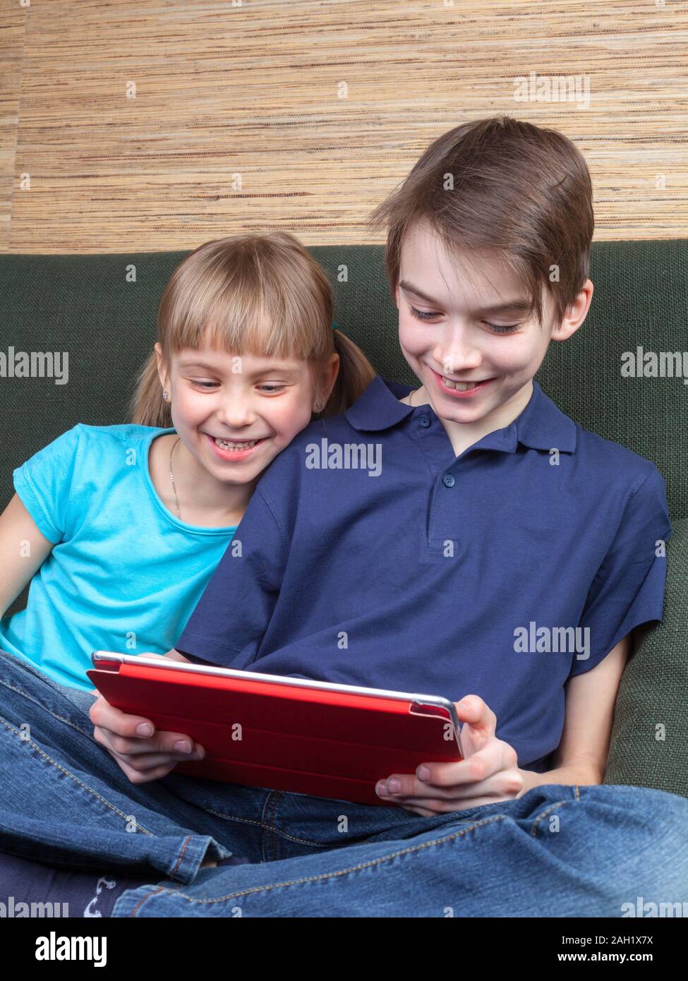 Kinder legere Kleidung spielen oder einen Film auf einem Touch Pad zu Hause sitzt auf einem grünen Sofa. Junge und Mädchen sind Halbgeschwister. Bruder ist Stockfoto