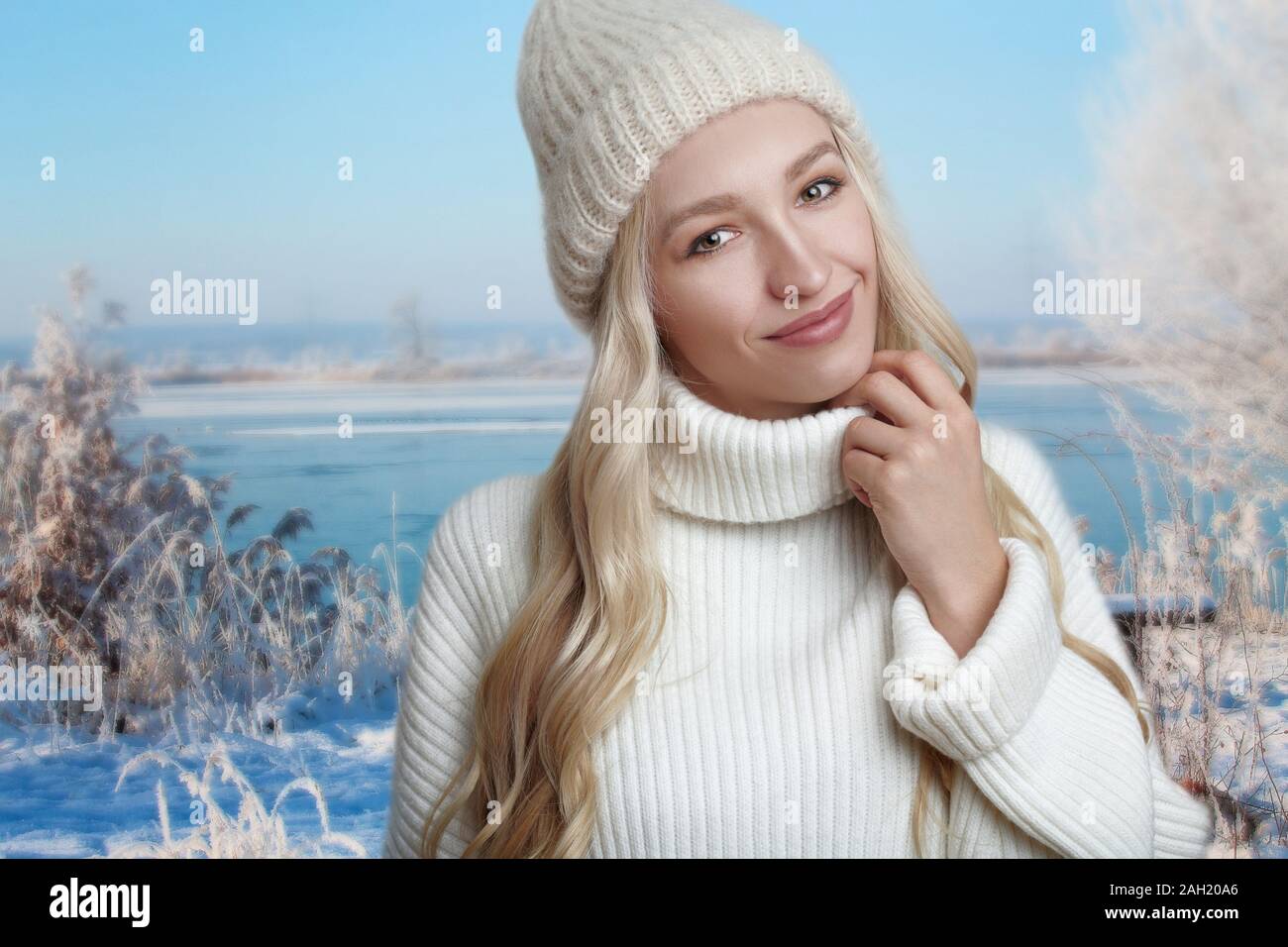 Junge blonde Frau, die ihre weißen Strickpullover genießen, gegen Winter Landschaft Hintergrund stehend, mit ihren Händen an ihrem Pullover Stockfoto