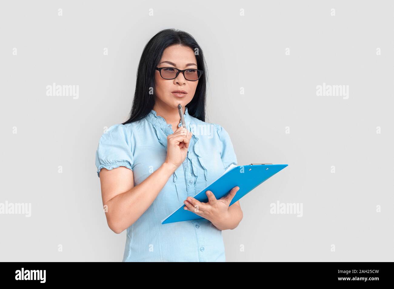 Freestyle. Asiatische Frau in Brillen isoliert auf Weiss mit Zwischenablage und Pen nachdenklich stehen Stockfoto