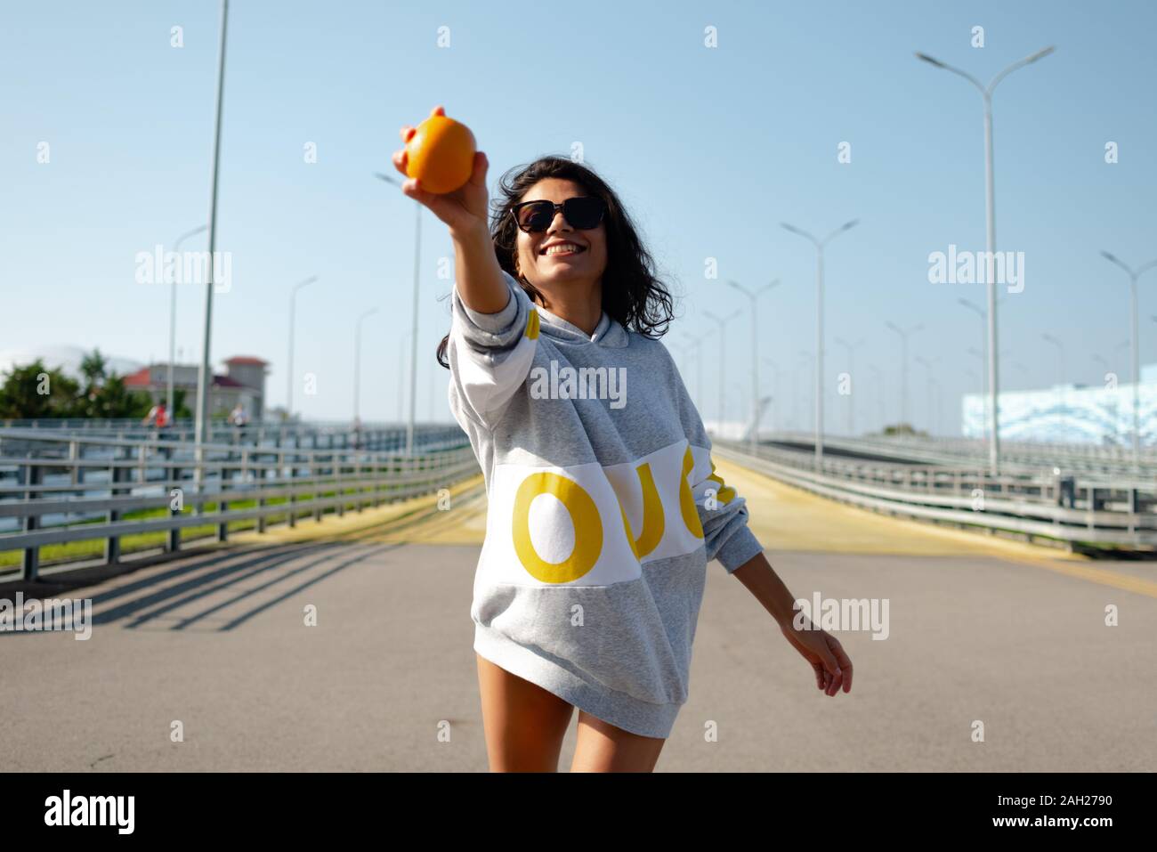 Ein Mädchen in einem Sport Hoodie wirft eine Orange wie ein Baseball. Sport, Fitness Stockfoto