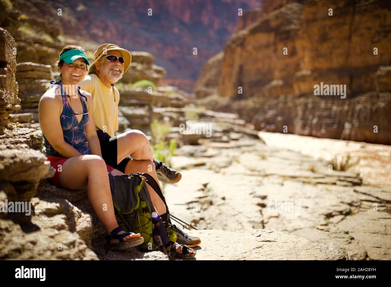 Porträt eines lächelnden jungen Frau und reifer Mann nebeneinander sitzen auf einem Felsen in der Nähe eines Flussufers eine Schlucht. Stockfoto