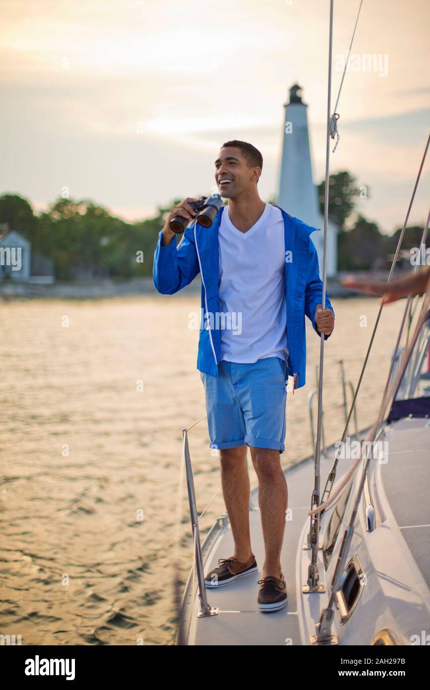 Gerne Mitte der erwachsene Mann mit Fernglas auf einem Segelboot bei Sonnenuntergang Stockfoto