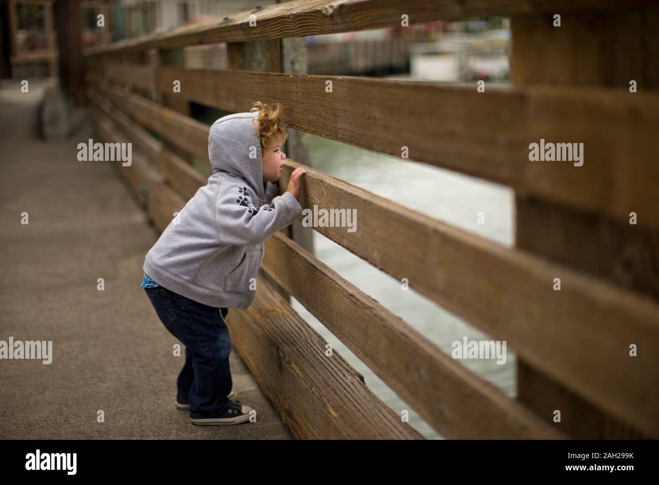 Neugierige kleine Junge spähen durch einen Zaun an der Waterfront Stockfoto