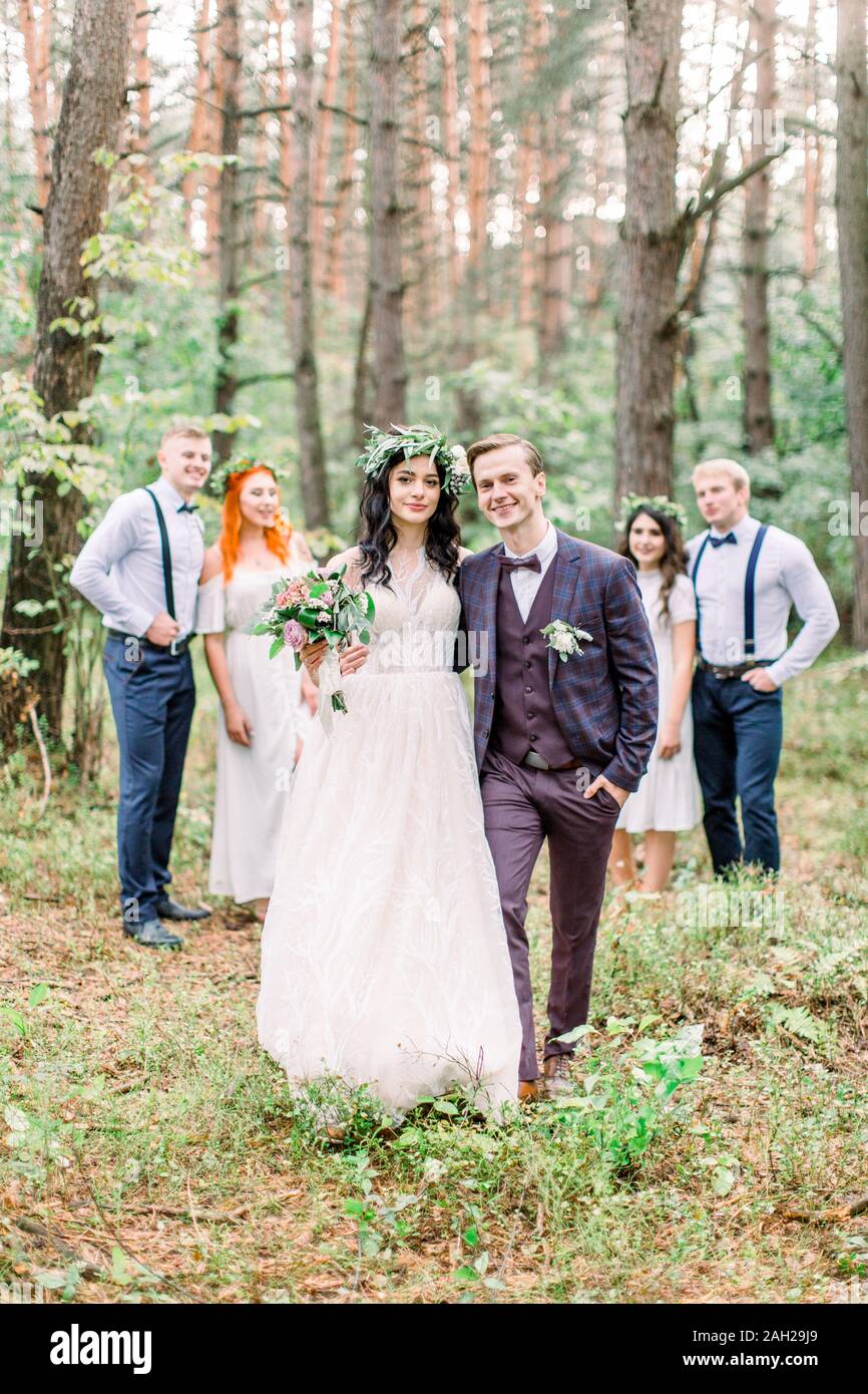 Glücklich lächelnde Brautpaar Hochzeit Kleidung tragen im rustikalen Stil  und ihre Freunde stehen Seite an Seite in einem Pinienwald Stockfotografie  - Alamy