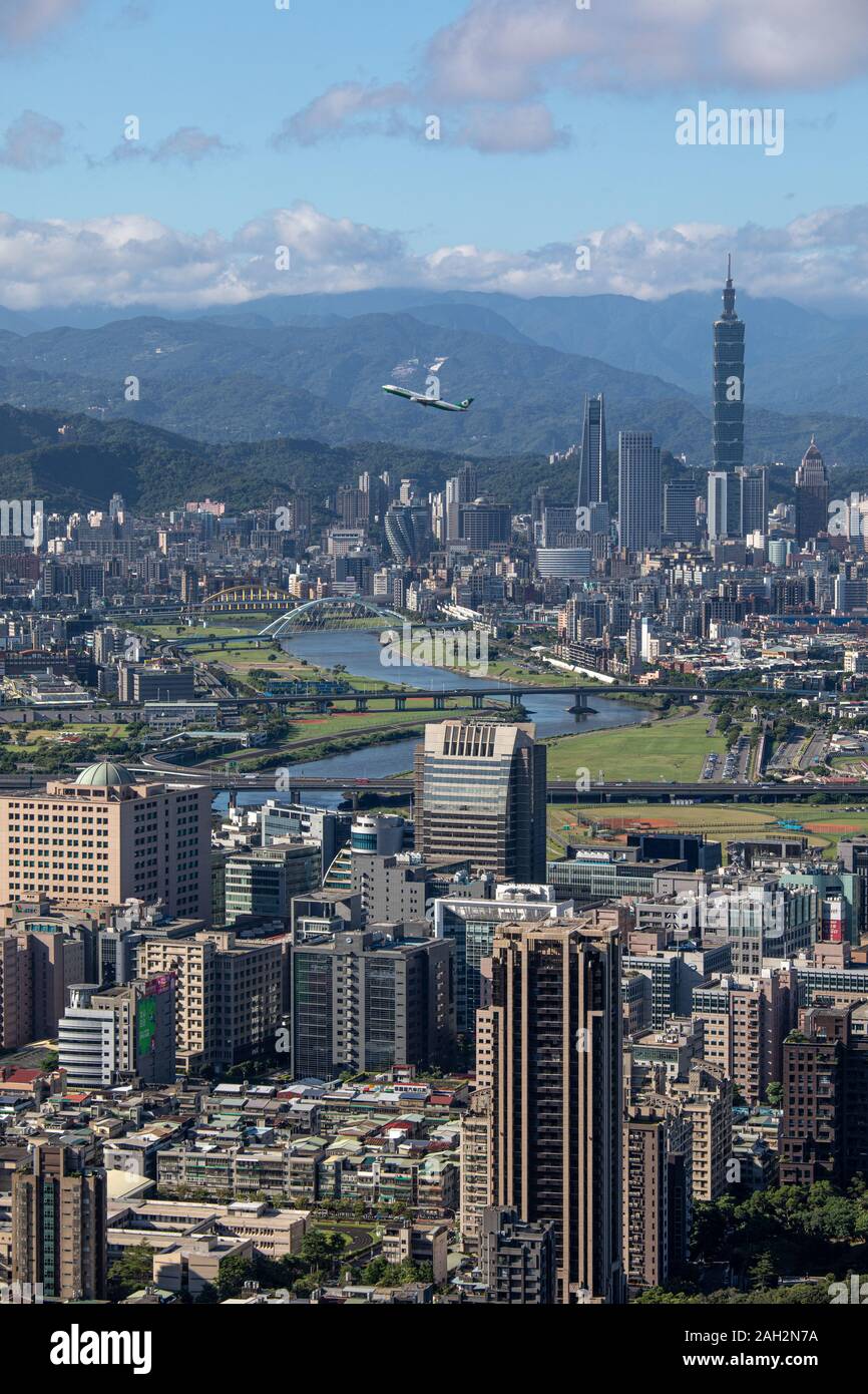 Ein Flugzeug startet von songshan International Airport und fliegt über Keelung River in Taipeh vor dem hintergrund der grünen Hügeln. Stockfoto