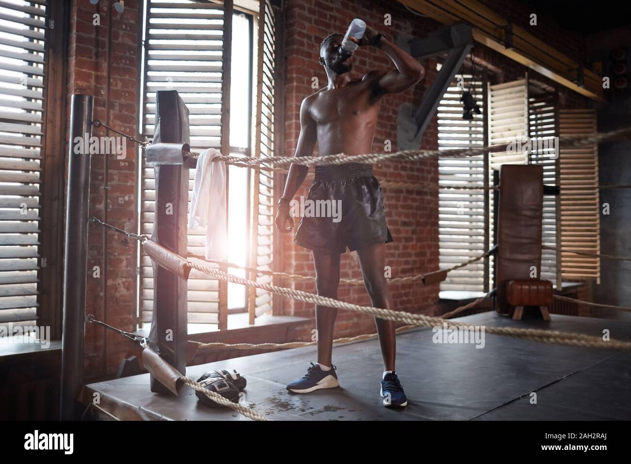 Afrikanische muskulösen Boxer Trinkwasser nach dem Sport Training beim Stehen auf Boxring in der Turnhalle Stockfoto
