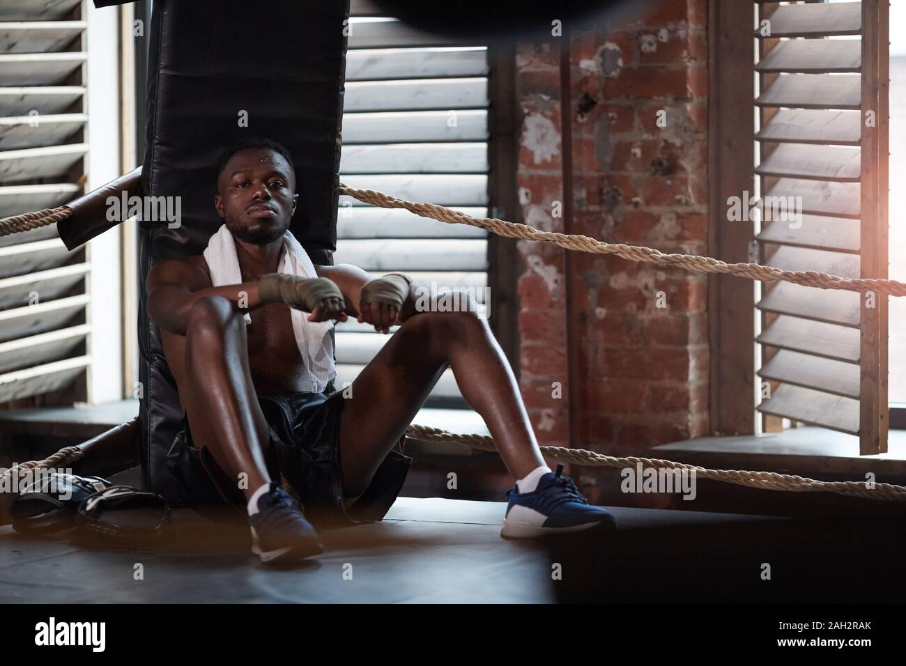 Portrait der Afrikanischen muskulösen Boxer auf Kamera, während sitzen auf dem Boden aufliegt und nach dem Sport Training Stockfoto