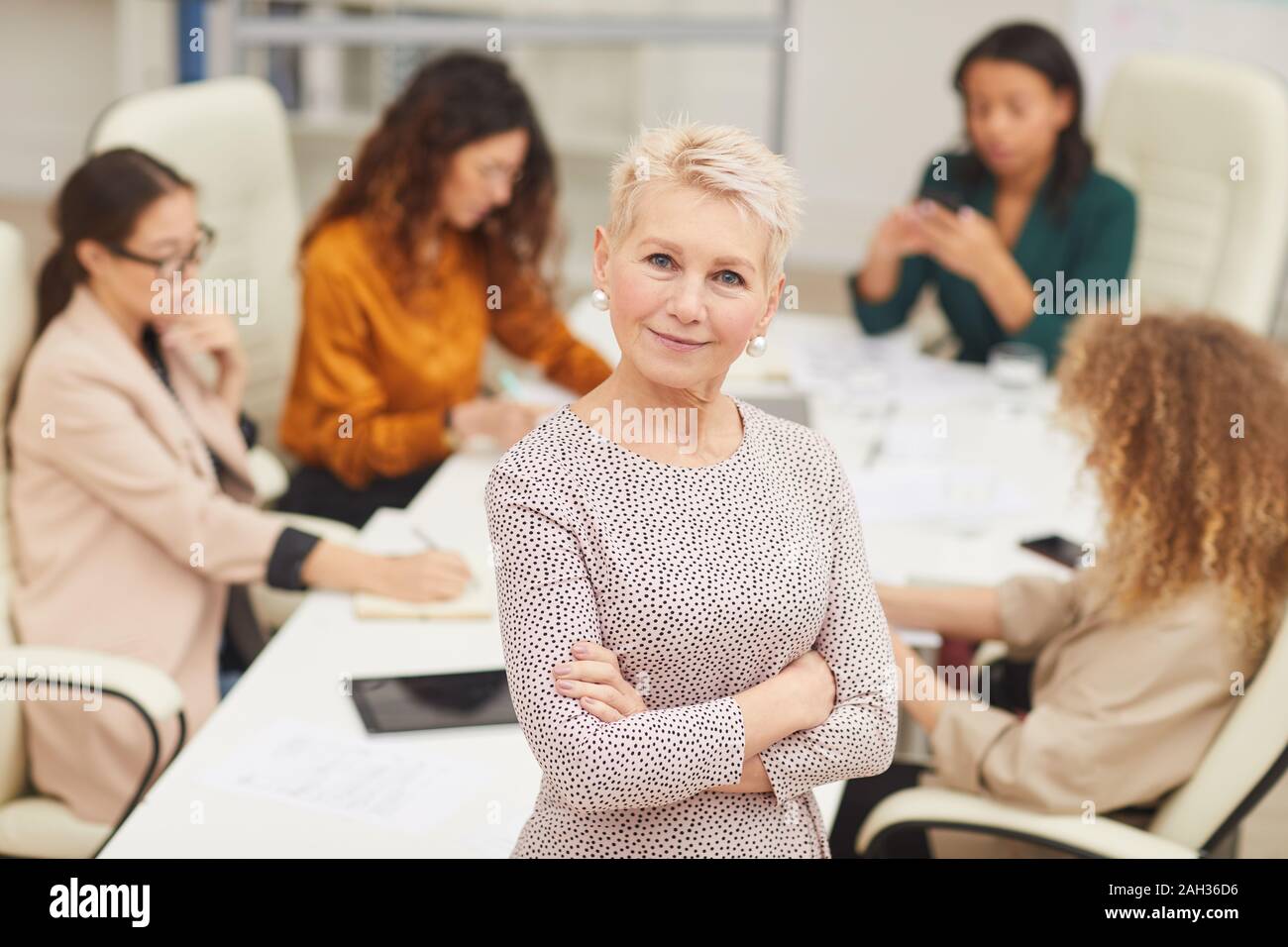 Zuversichtlich reife Frau stehend mit Arme geschlossen bei Kamera schaut lächelnd mit Kollegen hinter ihr Coworking, mittlere Portrait Stockfoto