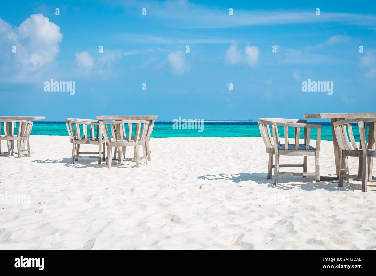 Stühle und Tische auf den weißen Strand der Malediven mit dem türkisblauen Meer im Hintergrund und Wolken am blauen Himmel Stockfoto