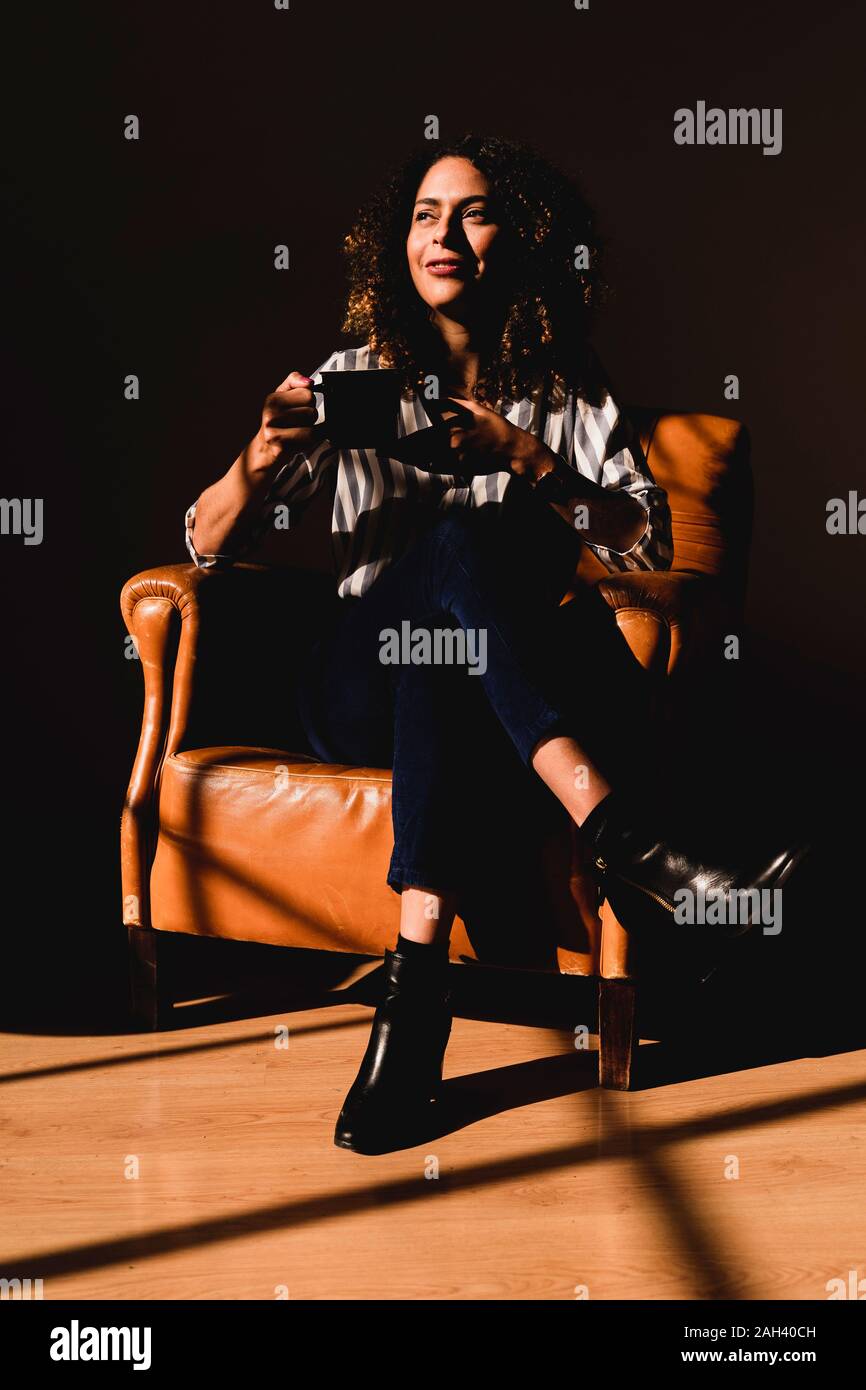 Frau in Leder Sessel mit Kaffeetasse sitzend Stockfoto