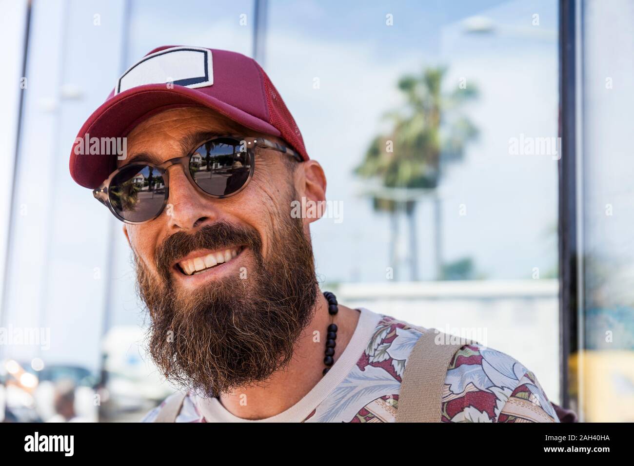 Lächelnd reifer Mann mit Bart, rote Kappe und Sonnenbrille Stockfoto