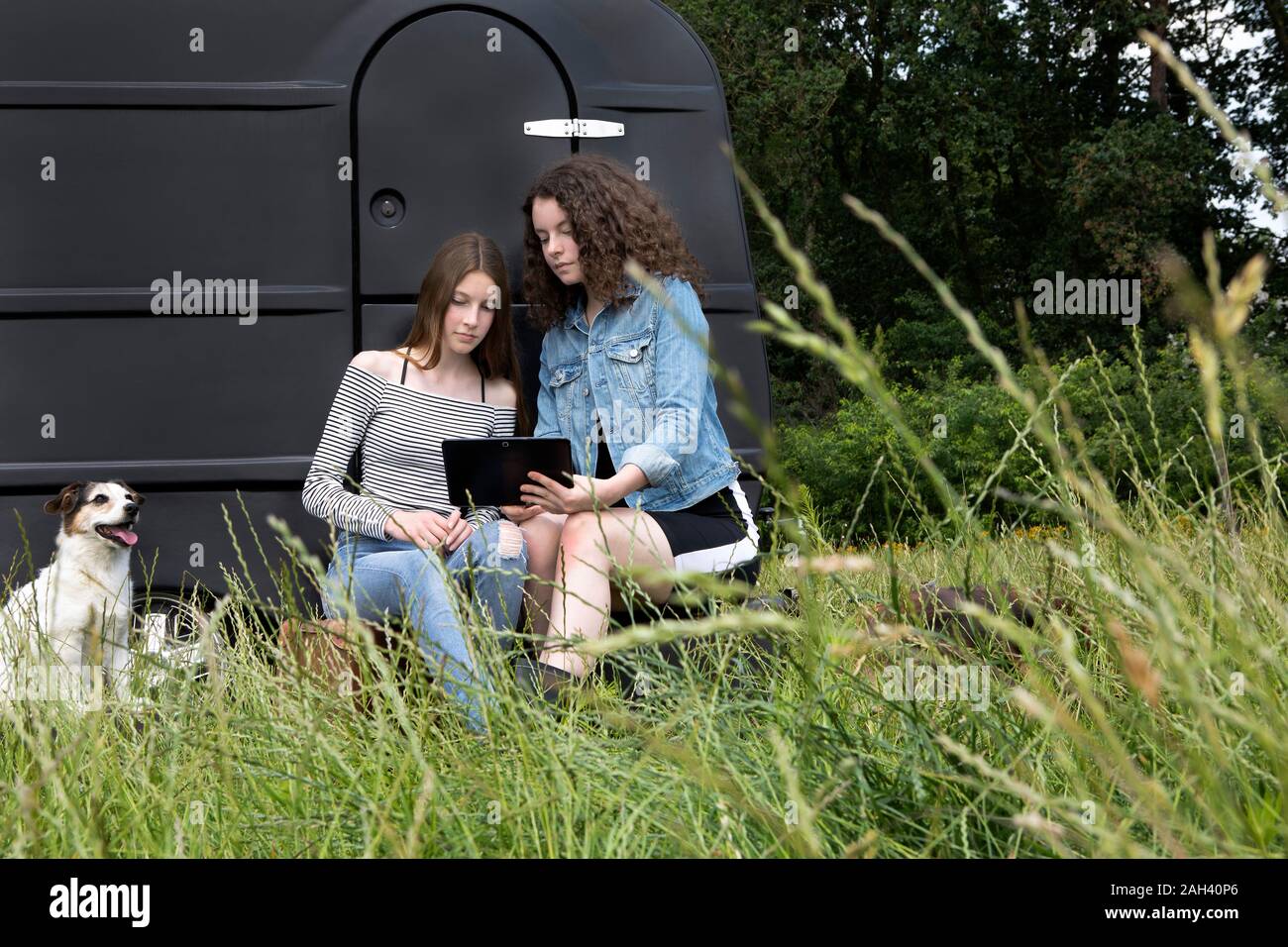 Zwei Freunde sitzen auf einer Wiese vor der schwarzen Caravan suchen Bei digital Tablet Stockfoto