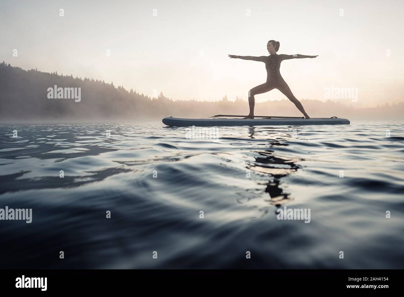 Frau üben paddle Board Yoga auf See Kirchsee am Morgen, Bad Tölz, Bayern, Deutschland Stockfoto