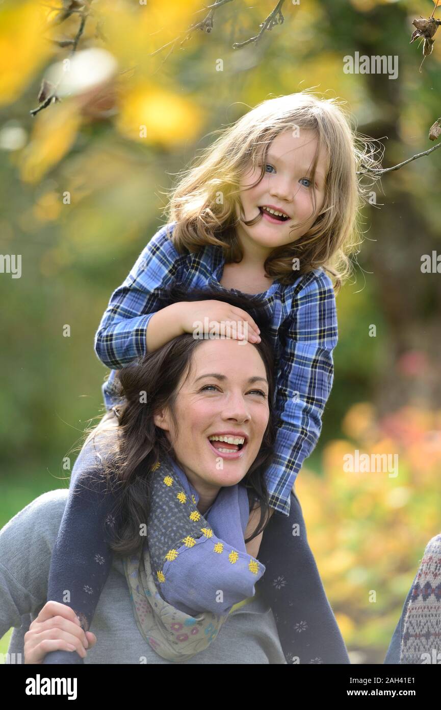 Tochter sitzen auf den Schultern der Mutter und Lachen Stockfoto