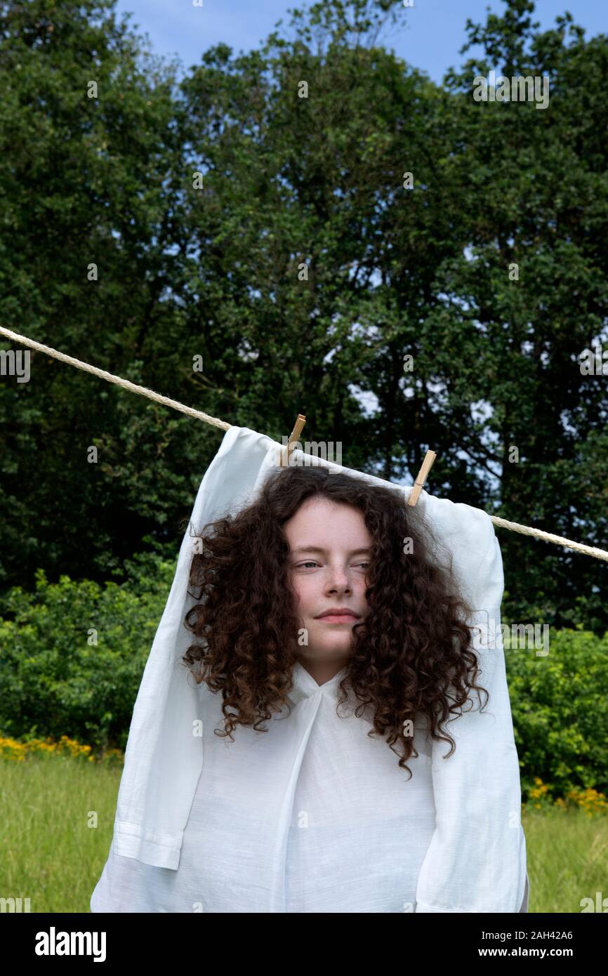 Porträt der jungen Frau mit braunen Korkenzieherlocken in weißem Kleid trocknen auf der Wäscheleine Stockfoto