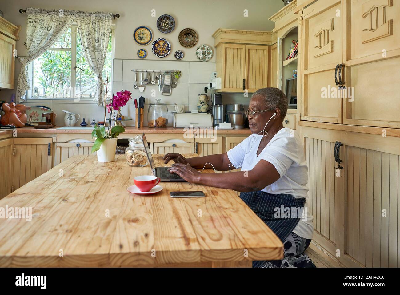 Ältere Frau am Küchentisch sitzen mit Laptop Stockfoto