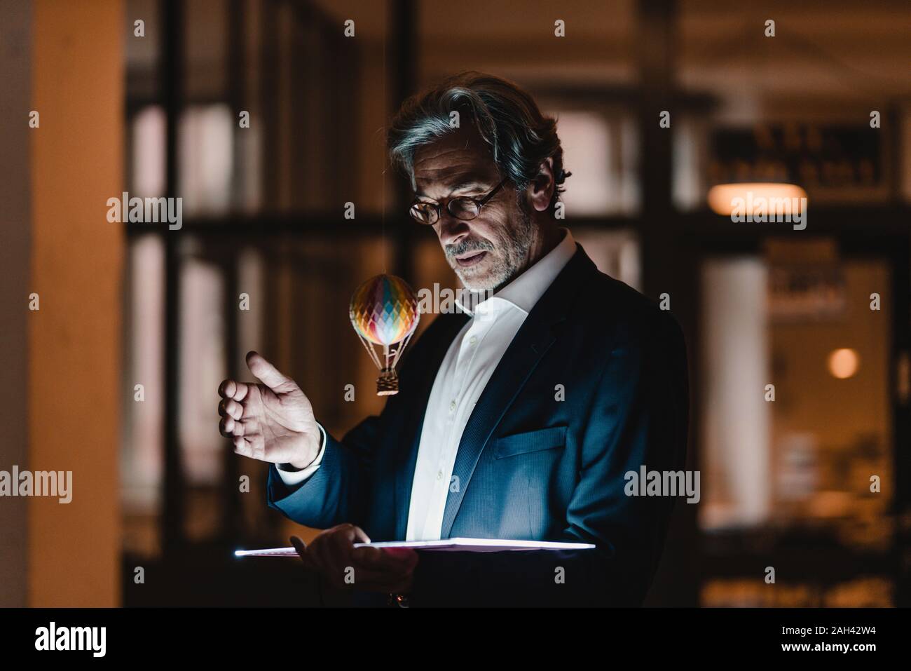 Senior Geschäftsmann mit Tablet und schwebenden Heißluftballon im Büro Stockfoto