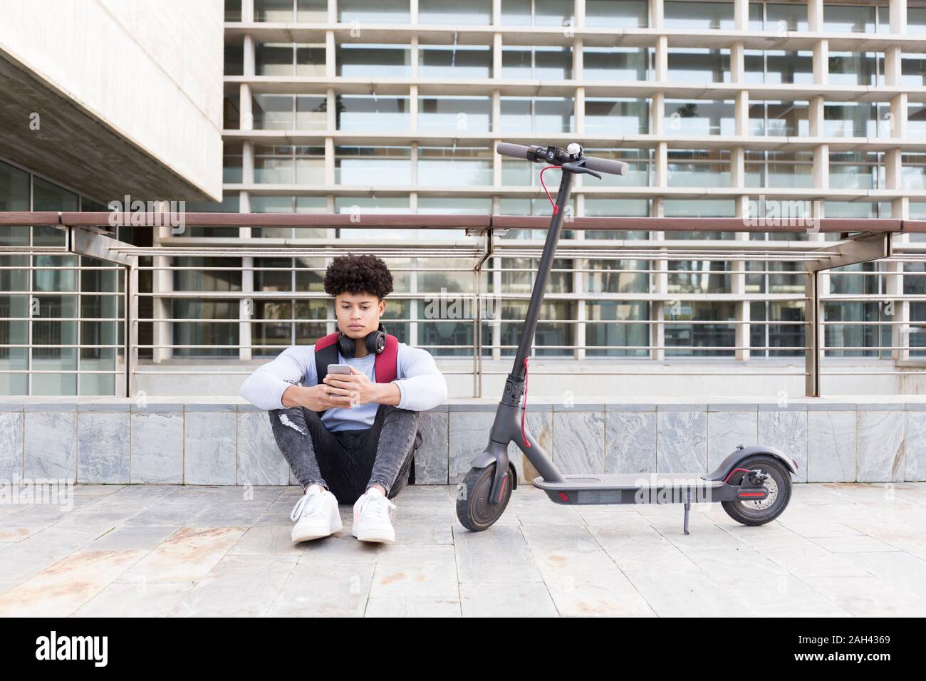 Junger Mann mit e-Scooter, entspannend und Sie ihr Smartphone Stockfoto