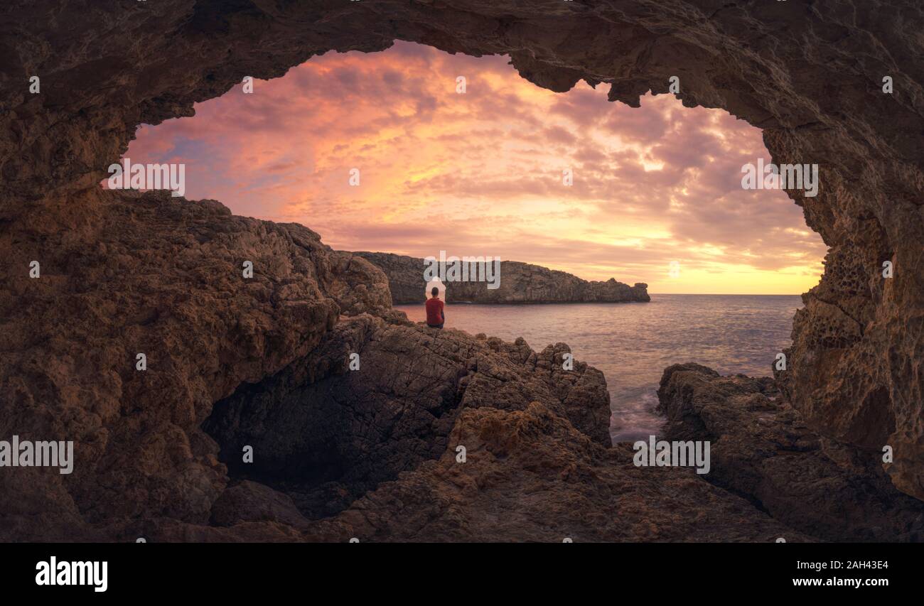 Ansicht der Rückseite des Mann sitzt auf Höhle bei Sonnenuntergang, Menorca, Spanien Stockfoto