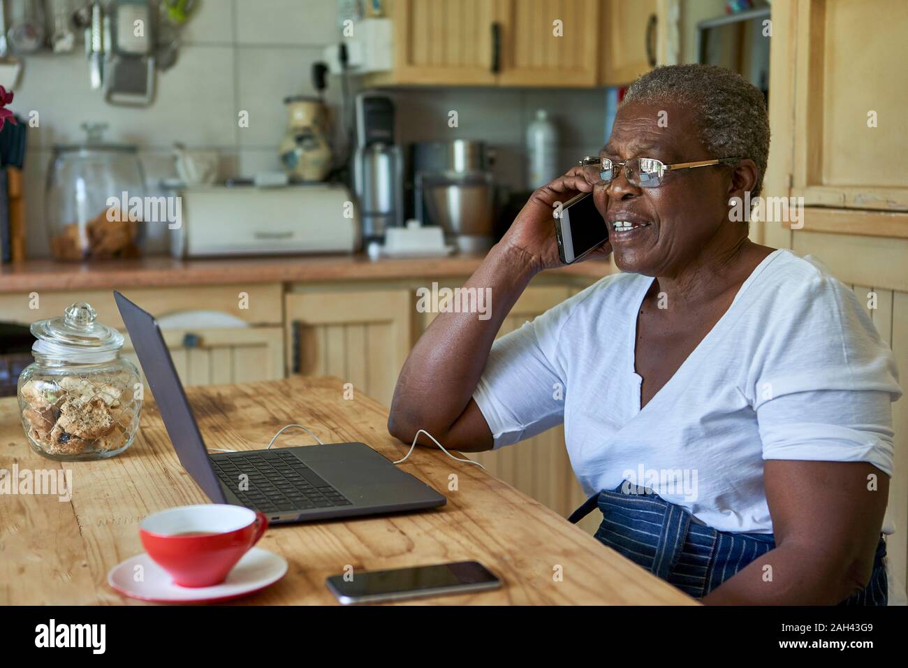 Ältere Frau am Küchentisch sitzen mit Laptop und Smartphone Stockfoto