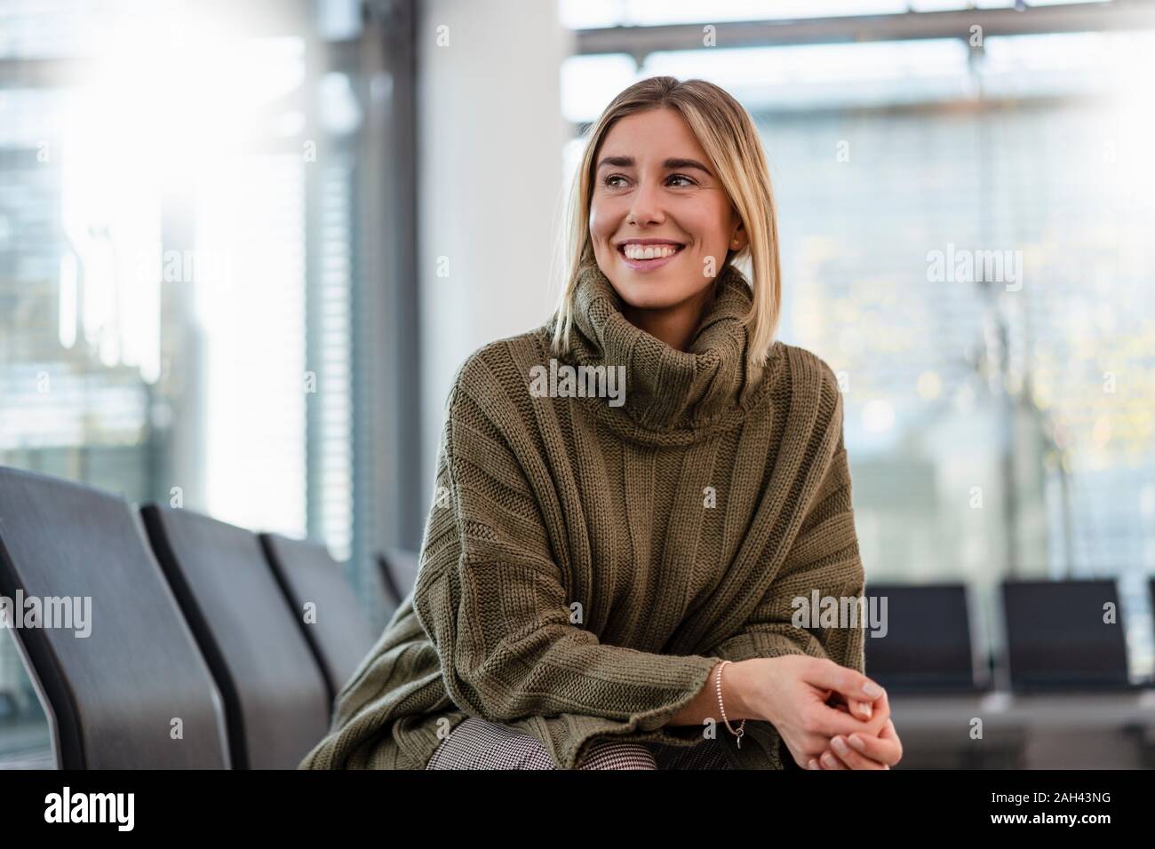 Lächelnde junge Frau sitzt im Wartebereich um suchen Stockfoto