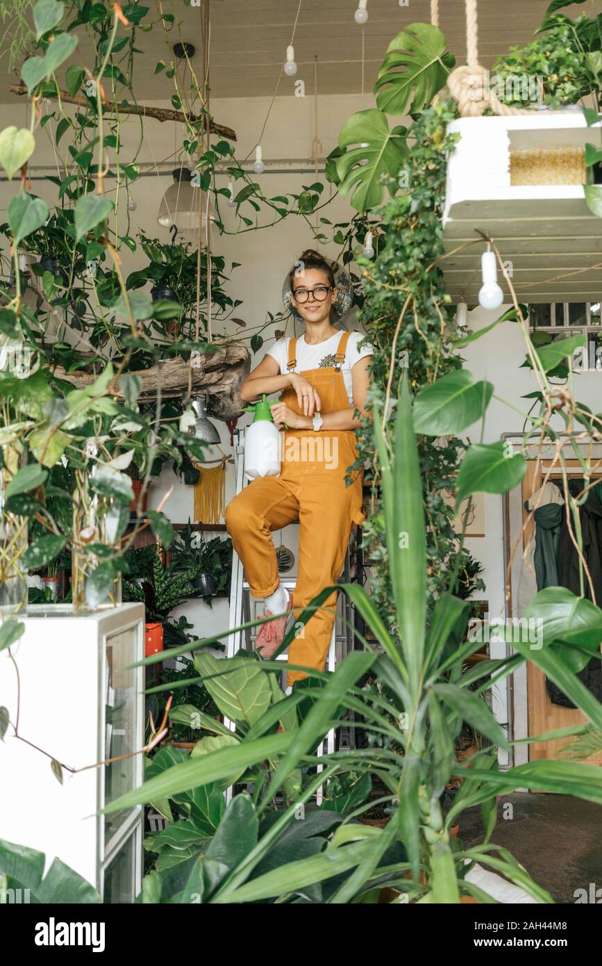 Portrait einer jungen Frau steht auf einer Leiter in einem kleinen Garten shop Stockfoto