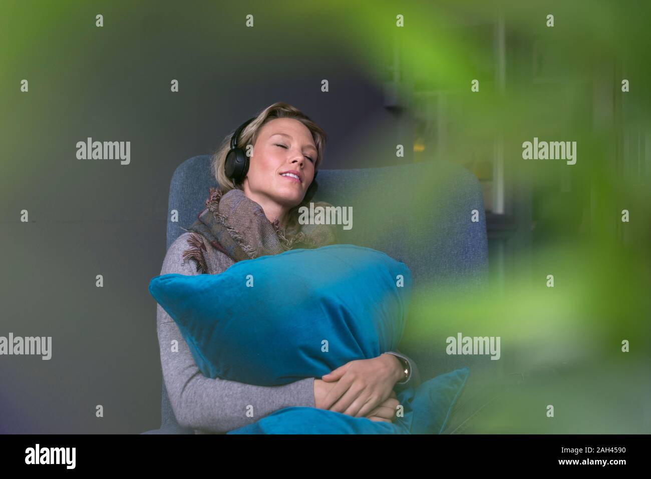 Junge Frau mit geschlossenen Augen im Sessel sitzen, Musik hören mit Kopfhörern Stockfoto