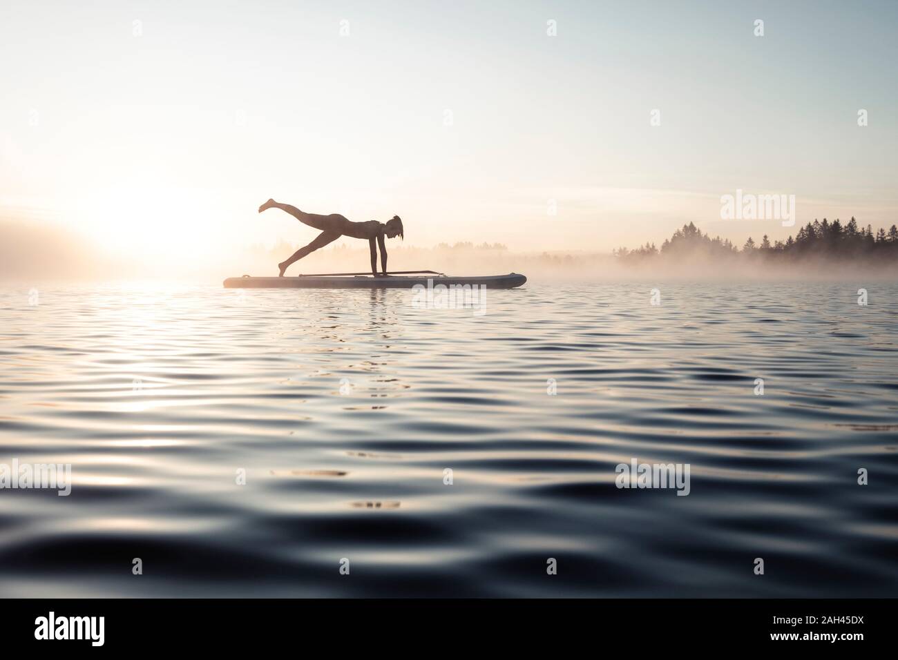 Frau üben paddle Board Yoga auf See Kirchsee am Morgen, Bad Tölz, Bayern, Deutschland Stockfoto