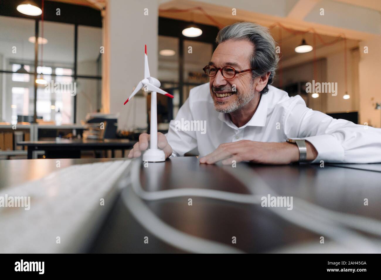 Gerne älteren Geschäftsmann mit wind turbine Modell im Büro Stockfoto